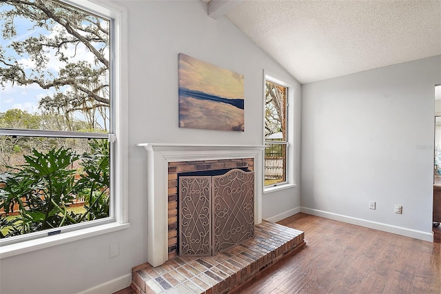 unfurnished living room featuring hardwood / wood-style flooring, a brick fireplace, vaulted ceiling with beams, and a textured ceiling