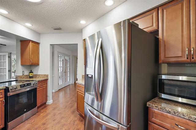 kitchen with appliances with stainless steel finishes, light hardwood / wood-style flooring, a textured ceiling, and dark stone countertops