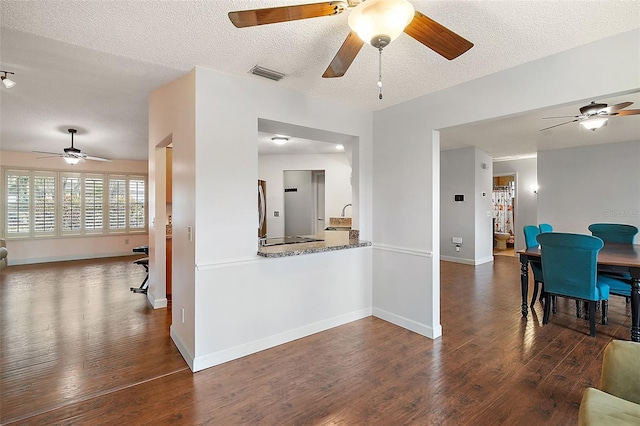 kitchen featuring light stone counters, dark hardwood / wood-style floors, kitchen peninsula, and a textured ceiling