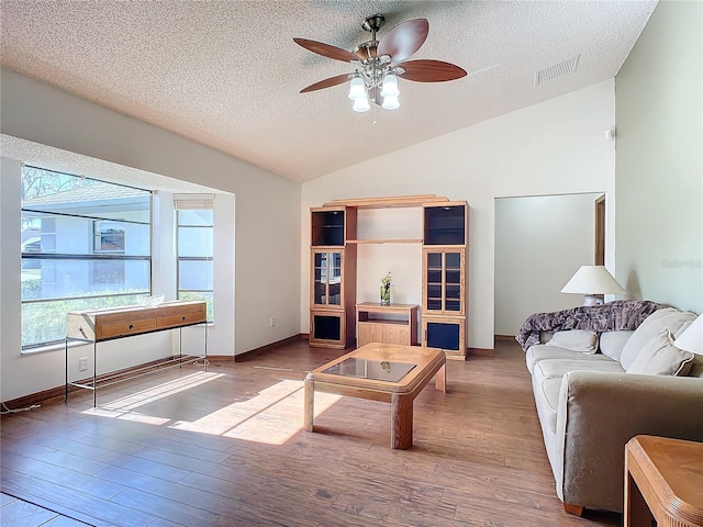 living room featuring ceiling fan, wood-type flooring, vaulted ceiling, and a textured ceiling