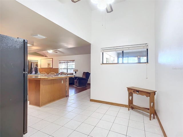 kitchen featuring ceiling fan, black refrigerator, light tile patterned flooring, vaulted ceiling, and kitchen peninsula