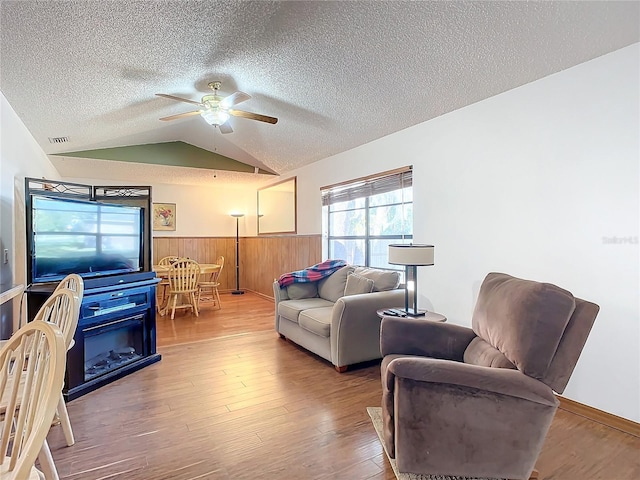 living room with hardwood / wood-style flooring, ceiling fan, vaulted ceiling, and a textured ceiling