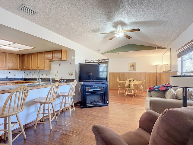 living room featuring lofted ceiling, sink, ceiling fan, a textured ceiling, and light hardwood / wood-style flooring