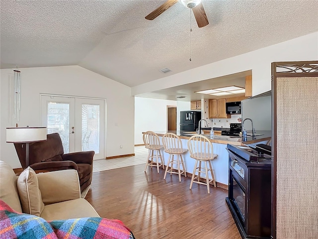 living room with lofted ceiling, sink, light hardwood / wood-style flooring, ceiling fan, and french doors