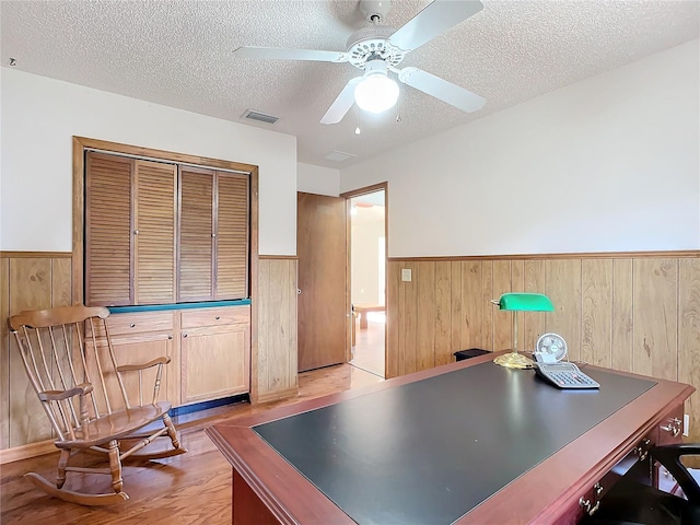 office with ceiling fan, wooden walls, a textured ceiling, and light hardwood / wood-style floors