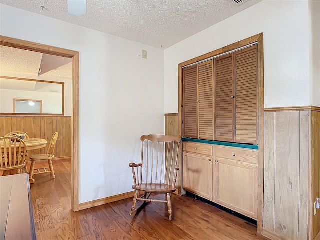 living area with wooden walls, a textured ceiling, and light wood-type flooring