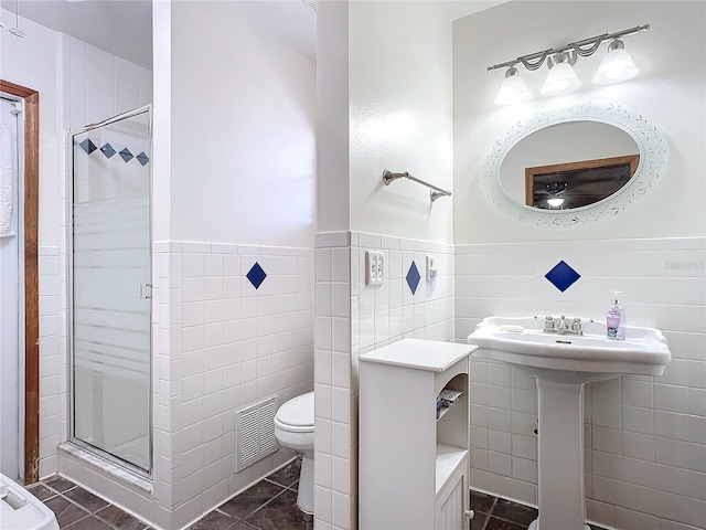 bathroom featuring toilet, a shower with shower door, tile patterned flooring, and tile walls