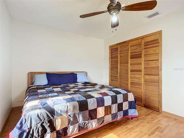 bedroom with a textured ceiling, light hardwood / wood-style flooring, a closet, and ceiling fan