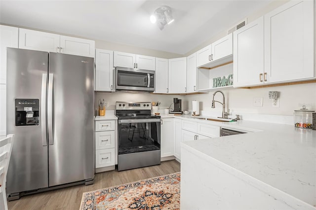 kitchen featuring sink, white cabinetry, light wood-type flooring, appliances with stainless steel finishes, and light stone countertops