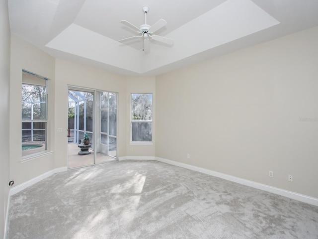 empty room featuring a raised ceiling, light colored carpet, and ceiling fan