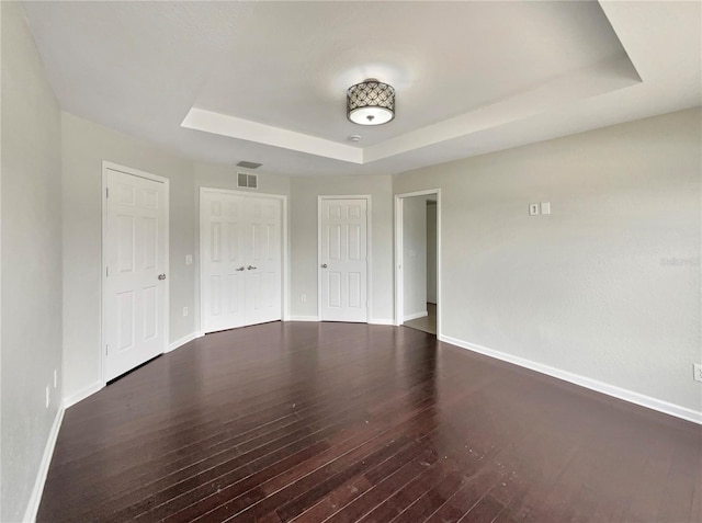 spare room featuring a tray ceiling and dark wood-type flooring