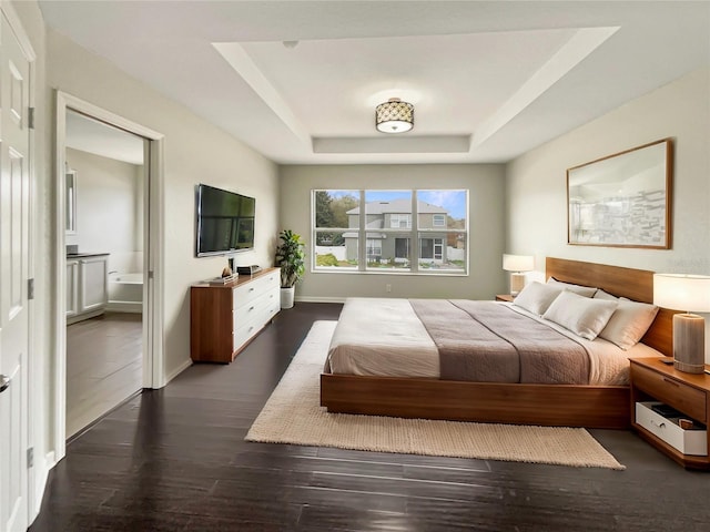 bedroom featuring dark wood-type flooring, connected bathroom, and a tray ceiling