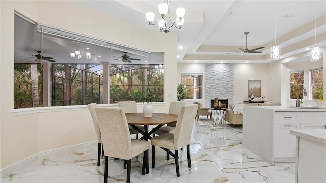 dining space featuring sink, a tray ceiling, and a stone fireplace