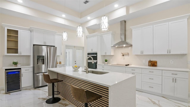 kitchen with beverage cooler, a kitchen breakfast bar, hanging light fixtures, black appliances, and wall chimney range hood