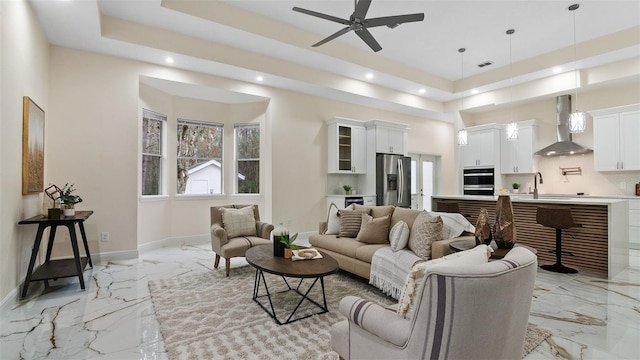 living room featuring sink, ceiling fan, and a tray ceiling