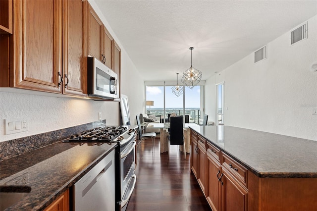 kitchen with dark wood-type flooring, stainless steel appliances, a textured ceiling, decorative light fixtures, and a chandelier