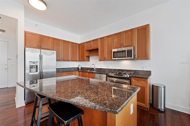 kitchen with sink, dark wood-type flooring, appliances with stainless steel finishes, a kitchen breakfast bar, and a center island