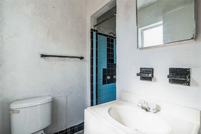 bathroom featuring sink, tiled shower, and toilet