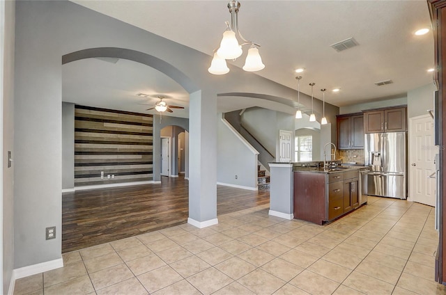 kitchen with a center island with sink, stainless steel refrigerator with ice dispenser, decorative light fixtures, light tile patterned flooring, and sink