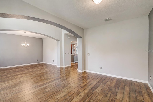 empty room featuring a chandelier, wood-type flooring, and a textured ceiling