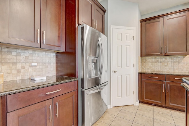 kitchen with light tile patterned flooring, dark stone countertops, backsplash, and stainless steel fridge with ice dispenser