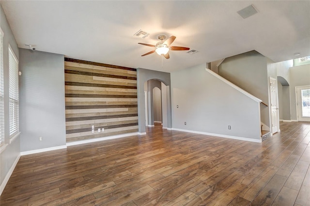 unfurnished living room featuring wooden walls, dark hardwood / wood-style floors, and ceiling fan