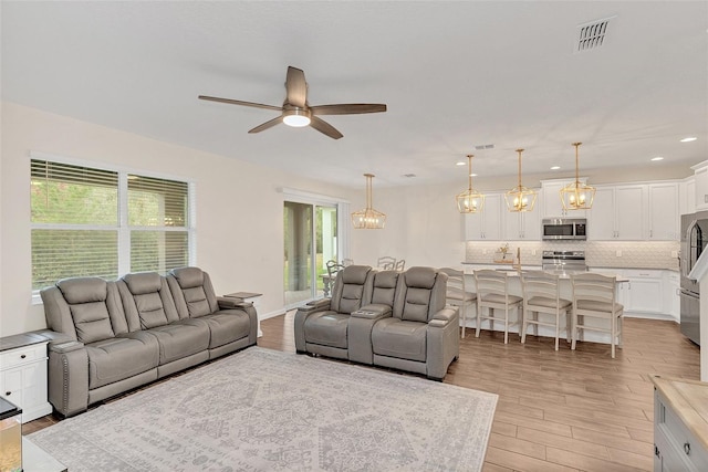 living room with ceiling fan with notable chandelier and light hardwood / wood-style flooring