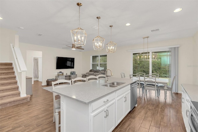 kitchen with pendant lighting, sink, dishwasher, white cabinetry, and a center island with sink