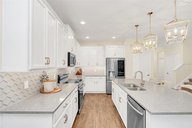 kitchen featuring decorative light fixtures, an island with sink, sink, white cabinets, and stainless steel appliances