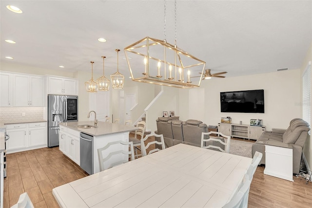 kitchen with decorative light fixtures, an island with sink, sink, backsplash, and stainless steel appliances