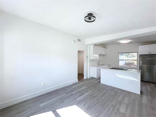 kitchen featuring sink, white cabinetry, stainless steel refrigerator, black electric cooktop, and hardwood / wood-style floors