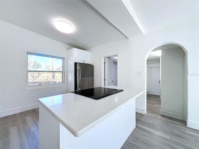 kitchen with stainless steel fridge, white cabinets, light stone counters, light hardwood / wood-style floors, and black electric cooktop