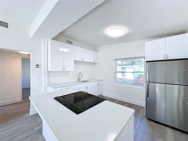 kitchen with black electric stovetop, stainless steel fridge, sink, and white cabinets