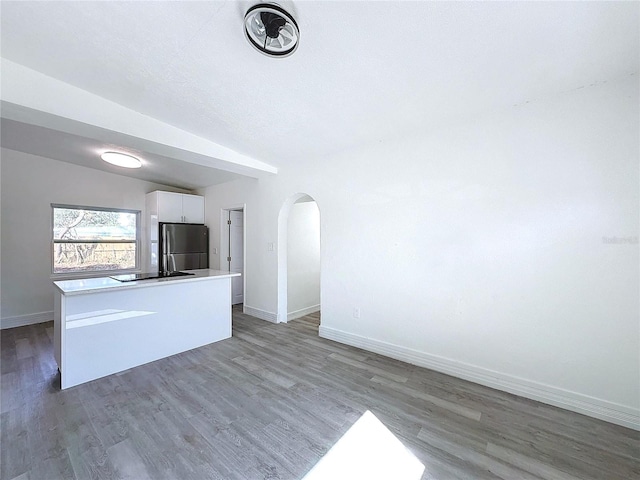 kitchen featuring white cabinets, vaulted ceiling, hardwood / wood-style floors, and stainless steel fridge