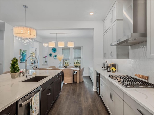 kitchen with stainless steel appliances, decorative light fixtures, sink, and wall chimney range hood