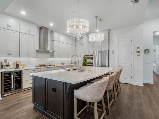 kitchen featuring sink, high end fridge, a kitchen island with sink, beverage cooler, and wall chimney exhaust hood