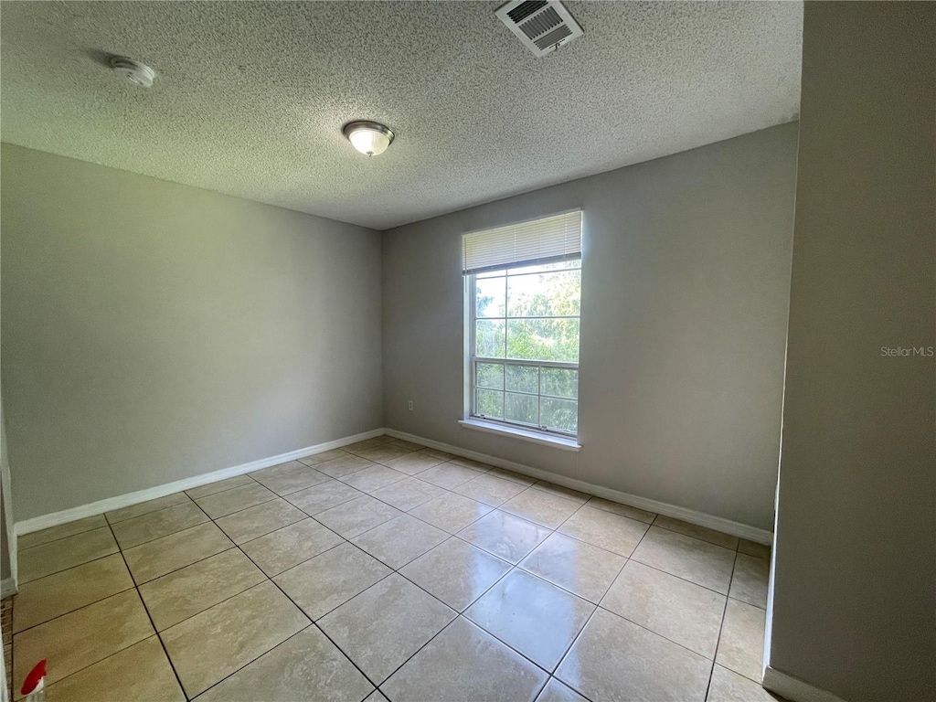 tiled empty room featuring a textured ceiling