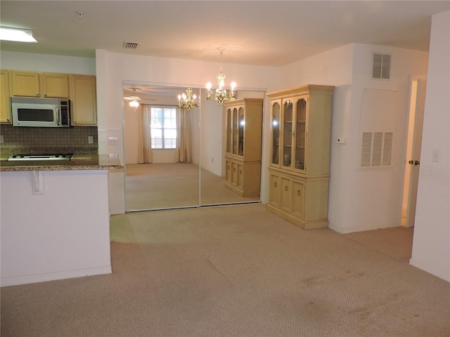 kitchen with ceiling fan with notable chandelier, pendant lighting, dark stone counters, decorative backsplash, and light colored carpet