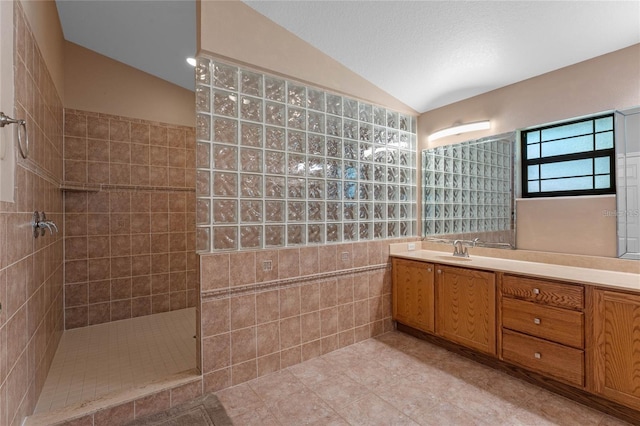 bathroom featuring tile patterned floors, vaulted ceiling, tile walls, a tile shower, and vanity