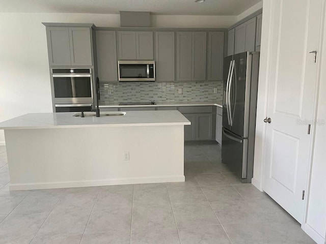 kitchen with sink, backsplash, stainless steel appliances, light stone countertops, and a center island with sink