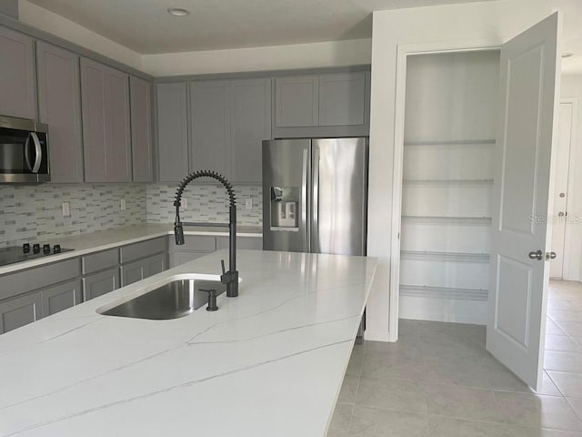 kitchen with sink, light tile patterned floors, gray cabinetry, stainless steel appliances, and light stone countertops