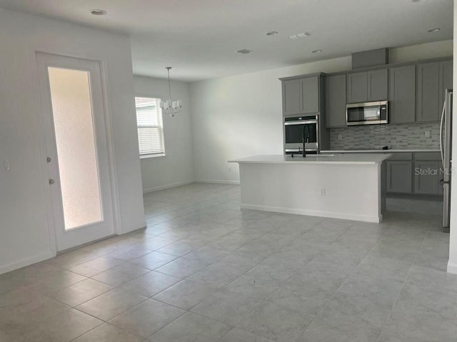 kitchen with pendant lighting, appliances with stainless steel finishes, gray cabinetry, tasteful backsplash, and an island with sink