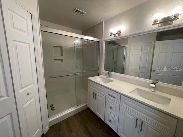 bathroom featuring vanity, wood-type flooring, an enclosed shower, and a textured ceiling