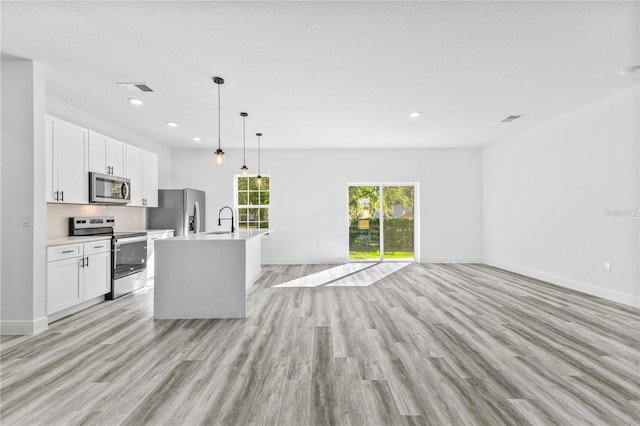 kitchen with sink, a kitchen island with sink, hanging light fixtures, stainless steel appliances, and white cabinets