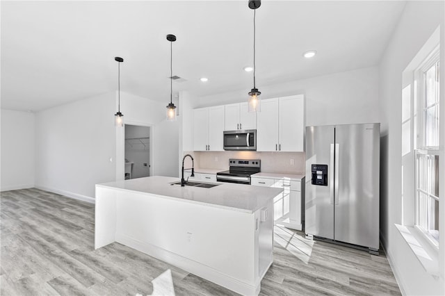 kitchen featuring appliances with stainless steel finishes, an island with sink, sink, white cabinets, and hanging light fixtures