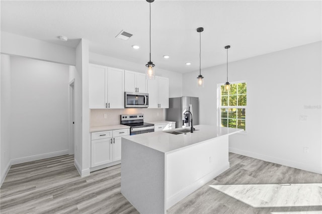 kitchen with white cabinetry, appliances with stainless steel finishes, a center island with sink, and decorative light fixtures