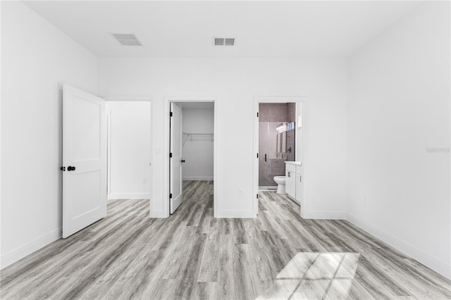 unfurnished bedroom with ensuite bath, a spacious closet, light hardwood / wood-style floors, and a closet