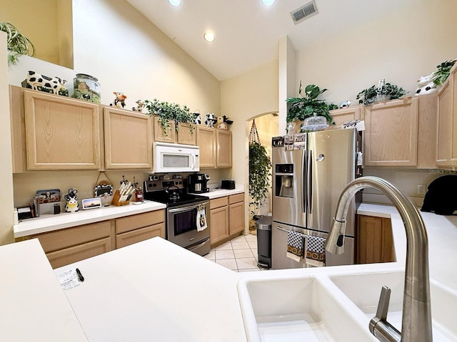 kitchen featuring sink, light tile patterned floors, stainless steel appliances, high vaulted ceiling, and light brown cabinetry