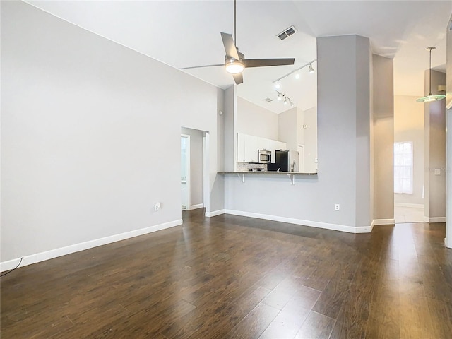 unfurnished living room featuring dark wood-type flooring, ceiling fan, rail lighting, and high vaulted ceiling