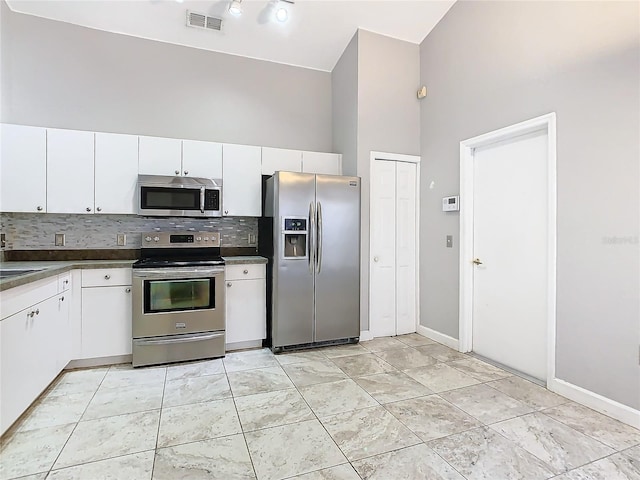 kitchen featuring a towering ceiling, appliances with stainless steel finishes, decorative backsplash, and white cabinets